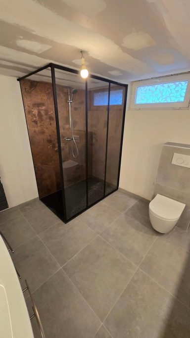Salle de bain moderne avec douche en verre et toilettes, carrelage gris.