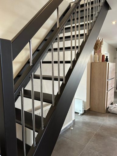 Escalier moderne en métal, avec des marches blanches et un mur gris en arrière-plan.